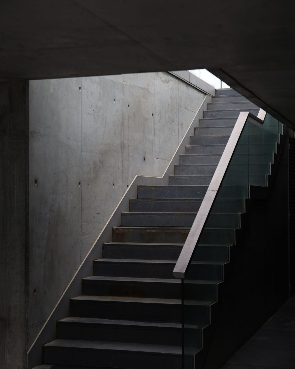 A cast concrete stair with a glass balustrade, lit from a skylight above