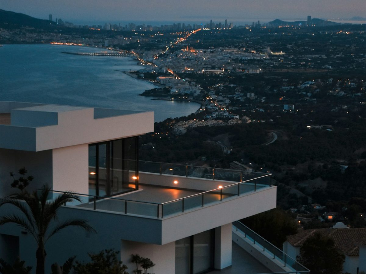 A modern rendered duplex on a sloping site, photographed at dusk with the city beyond